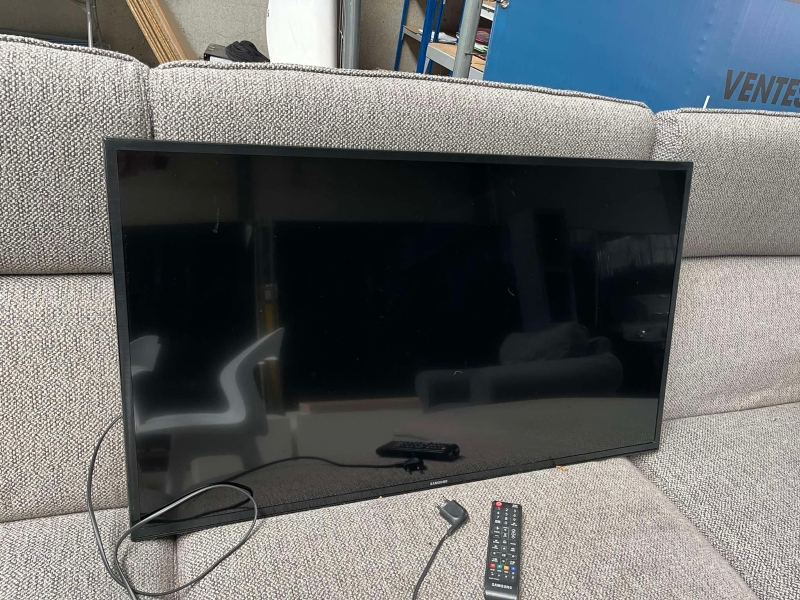 une télévision écran plat noire de marque SAMSUNG avec câble et deux télécommandes ; 50cm x 88,5cm, en bon état